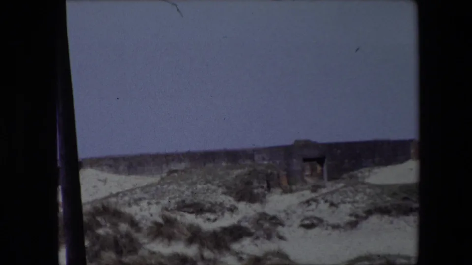 1967 Calais frame with a weathered low structure set into scrub-covered dunes, showing an open doorway-like dark recess and muted small-gauge film color.