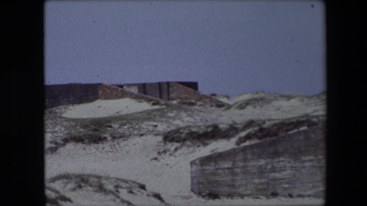 Concrete wall and sandy rockface with grass along the slope.