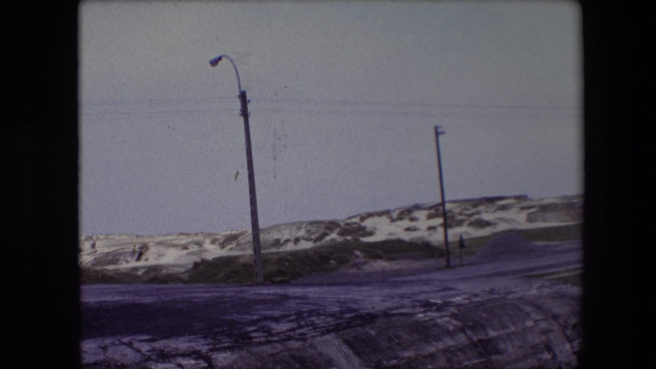 Road and dune landscape with streetlight, utility pole, snow patches, and pale sky.