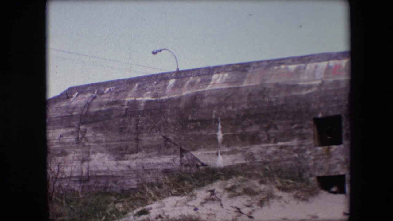 Concrete bunker wall with square openings and grass at the base.