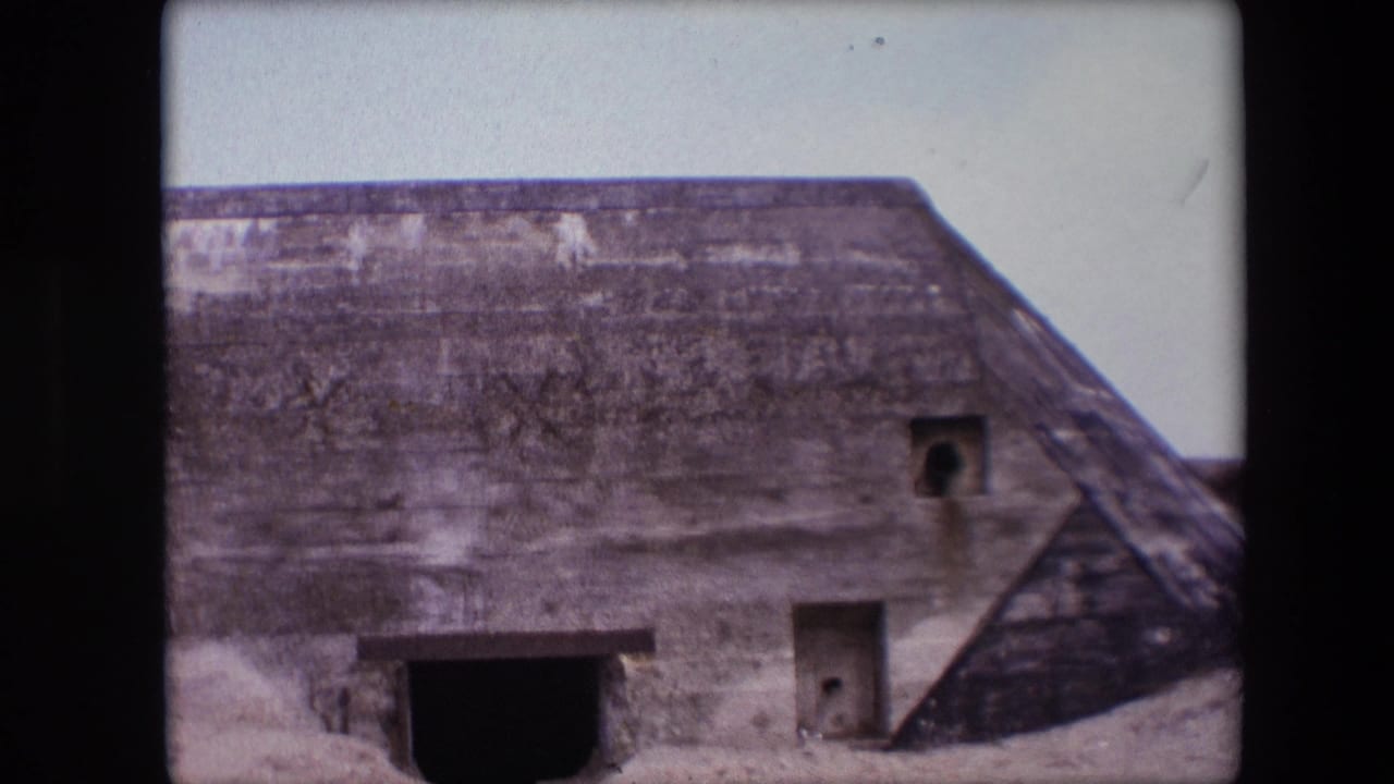Concrete beach bunker framed slightly farther right with a sloped side and dark doorway.