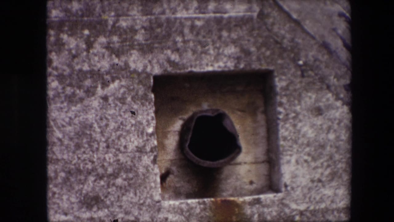 1967 Calais home-movie frame showing a weathered square concrete recess with a dark pipe-like opening and rough film edges.