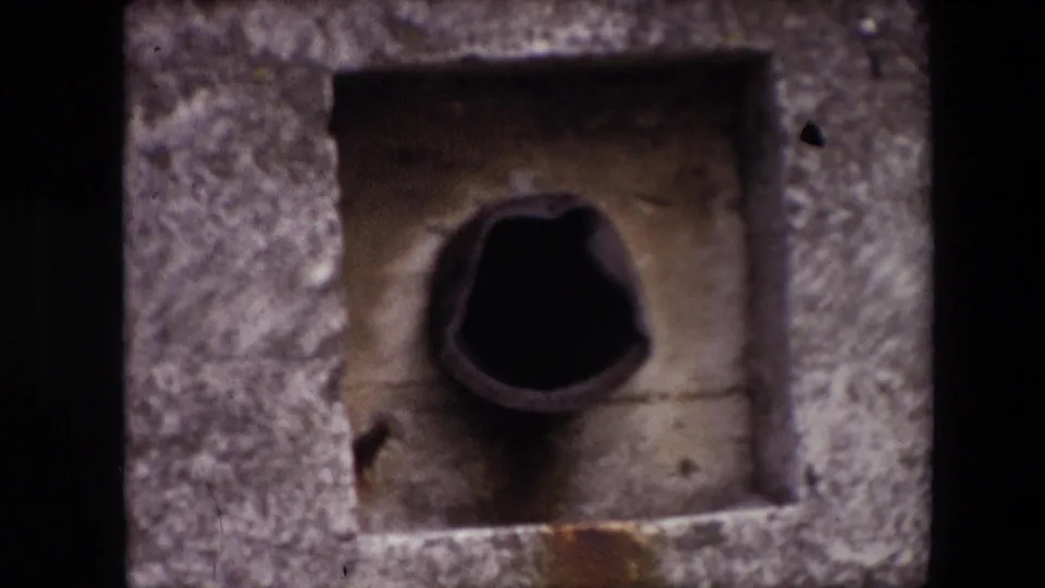 1967 Calais home-movie still showing the same weathered concrete recess, dark pipe-like center, and small stains around the lower edge.