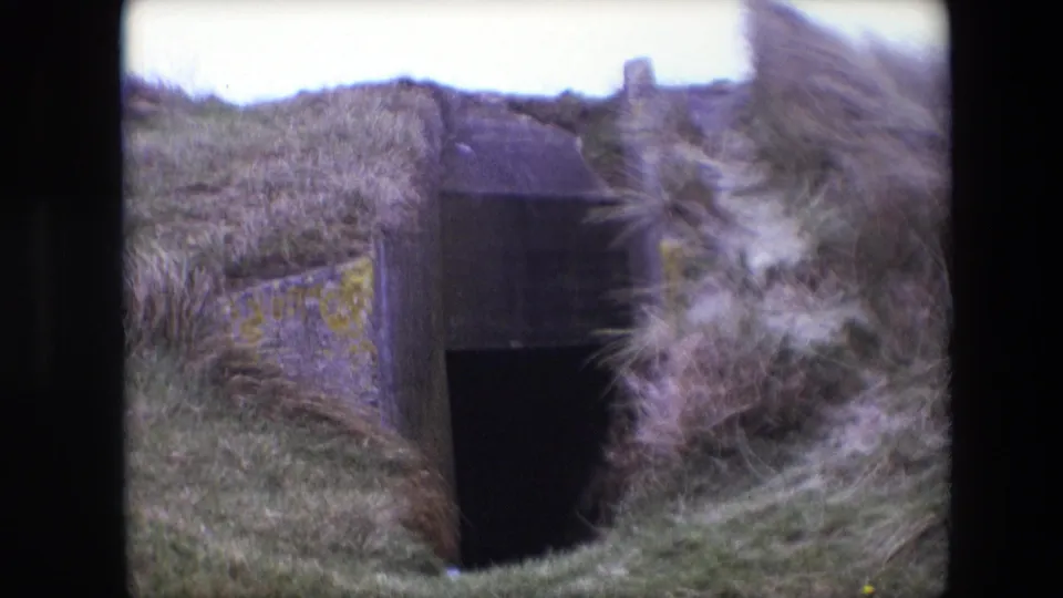 1967 Calais closing frame of a bunker-like concrete doorway in dunes, with tall grass sweeping across the right side of the 8mm frame.