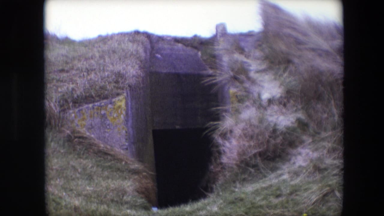 1967 Calais 8mm frame showing a weathered concrete tunnel or bunker-like entrance embedded in a grass-covered slope.