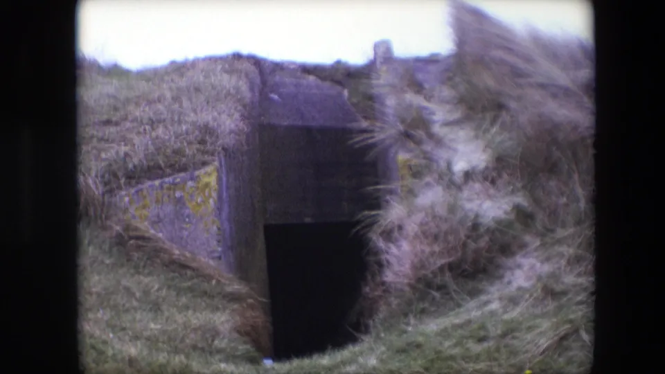 1967 Calais 8mm frame showing a weathered concrete tunnel or bunker-like entrance embedded in a grass-covered slope.