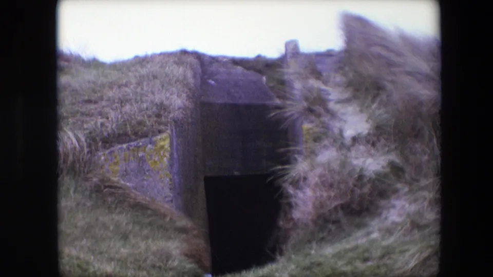 1967 Calais 8mm frame with wind-blown grass partly covering a weathered concrete entrance set into a slope.