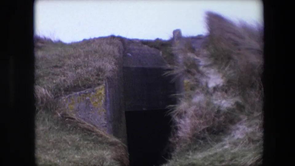 1967 Calais 8mm frame showing the entrance from a similar angle, with grass and dune vegetation obscuring part of the concrete structure.