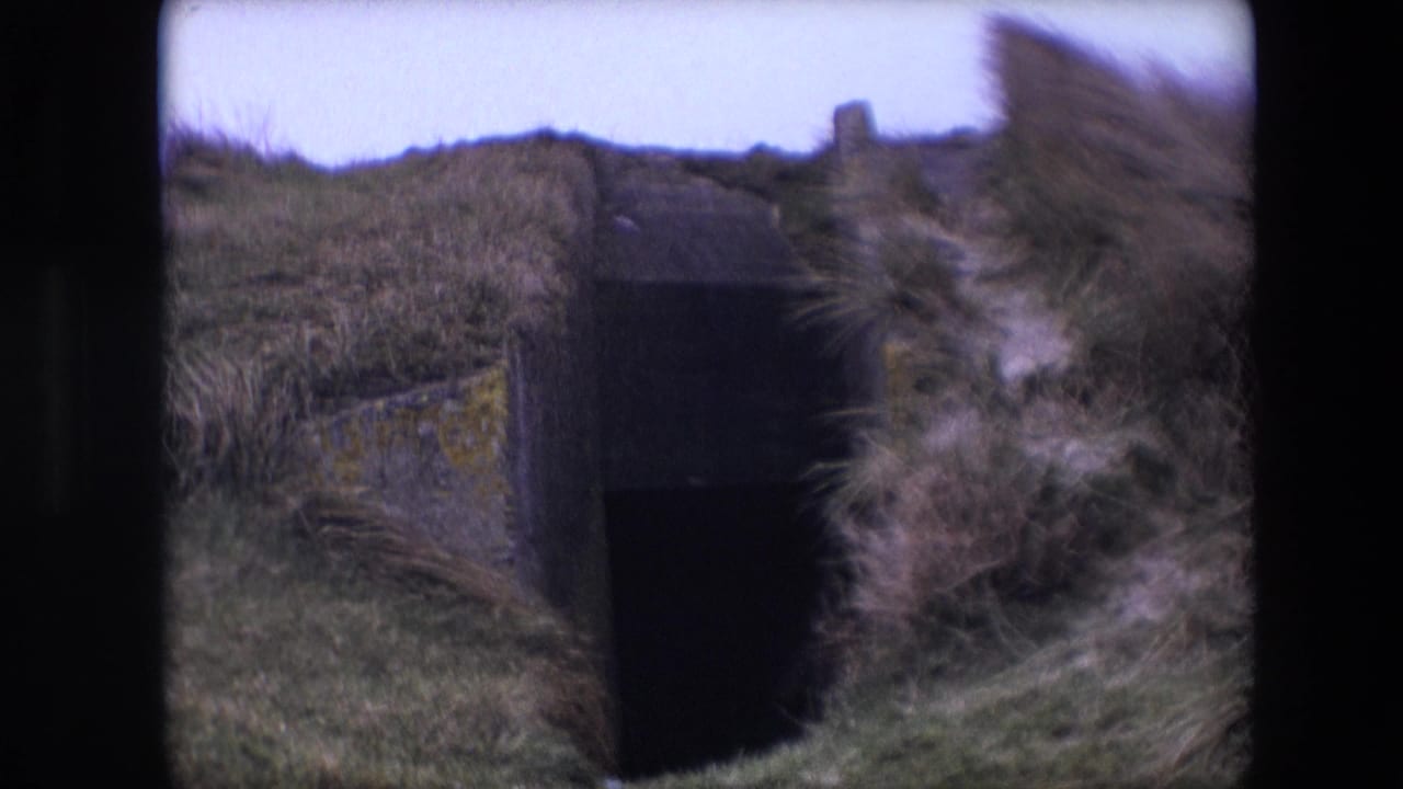 1967 8mm home-movie frame from the Calais, France clip showing a weathered concrete opening or bunker-like structure partly buried in grass.
