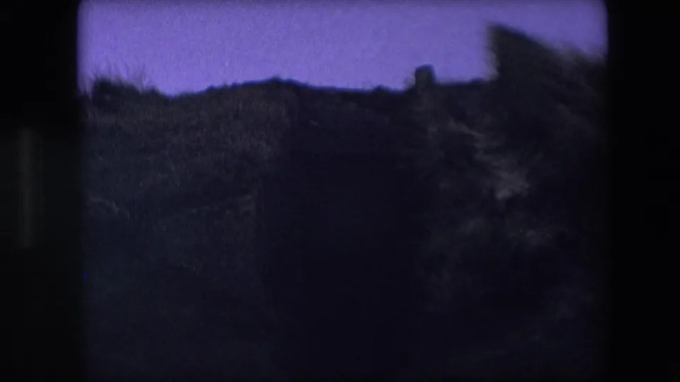 Dark, grainy 8mm frame from the 1967 Calais, France clip showing a silhouetted grassy hillside and faint sky with little readable detail.