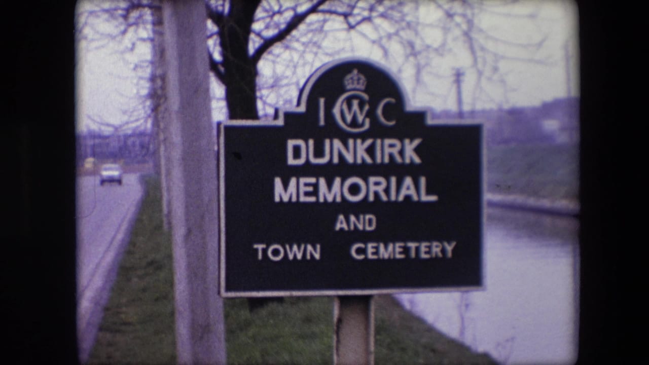 1967 8mm frame from France showing a black IWC Dunkirk Memorial and Town Cemetery sign near a roadside canal with bare trees behind it.