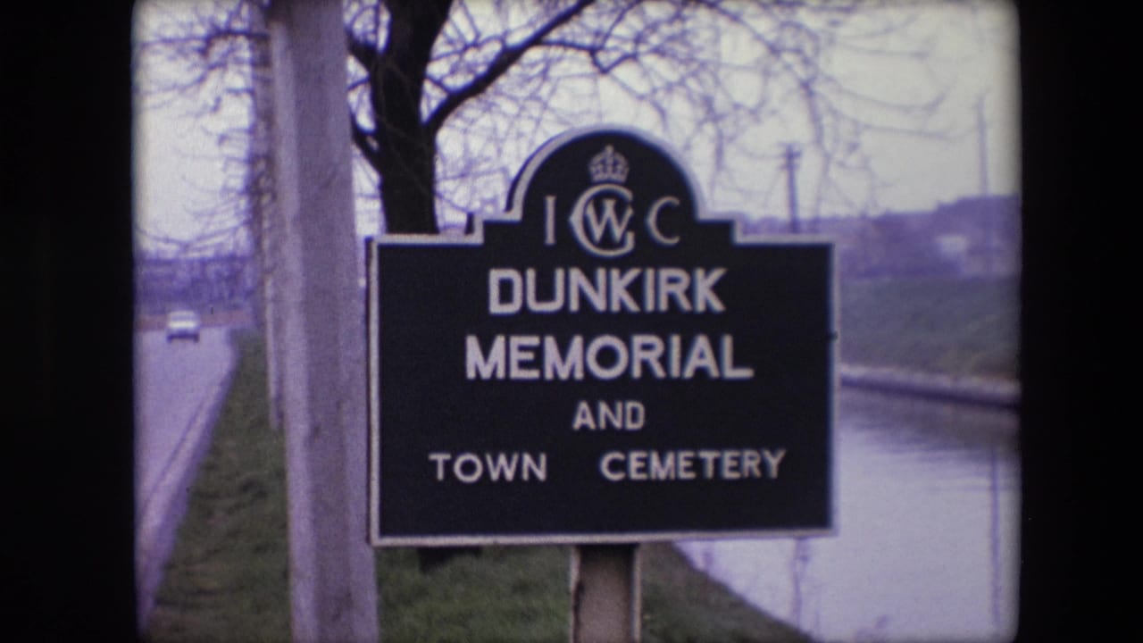 1967 8mm frame showing the Dunkirk Memorial and Town Cemetery sign beside a quiet road and canal, with a small car visible in the distance.