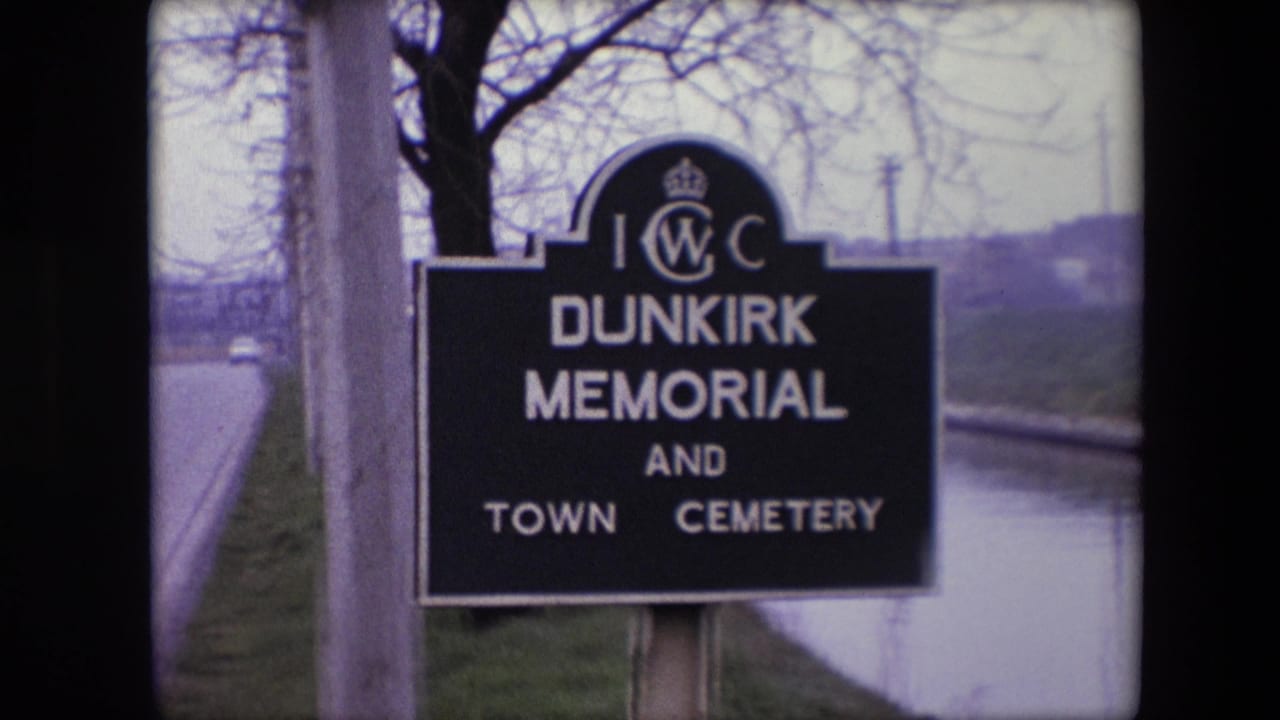1967 8mm frame from Calais, France showing the Dunkirk Memorial and Town Cemetery sign beside a quiet roadside with bare trees in the background.