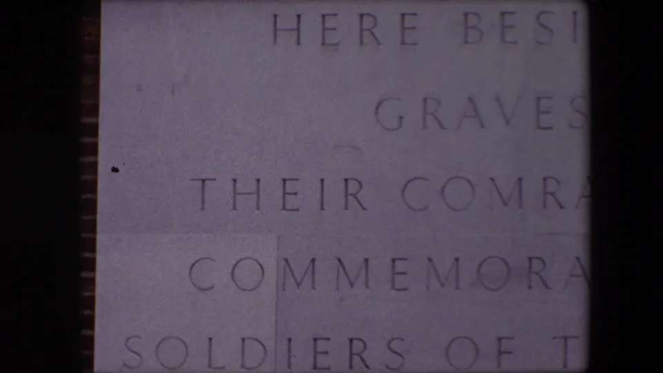 Close-up 1967 8mm frame of the Dunkirk memorial stone with partial engraved text referring to graves, comrades, commemoration, and soldiers.