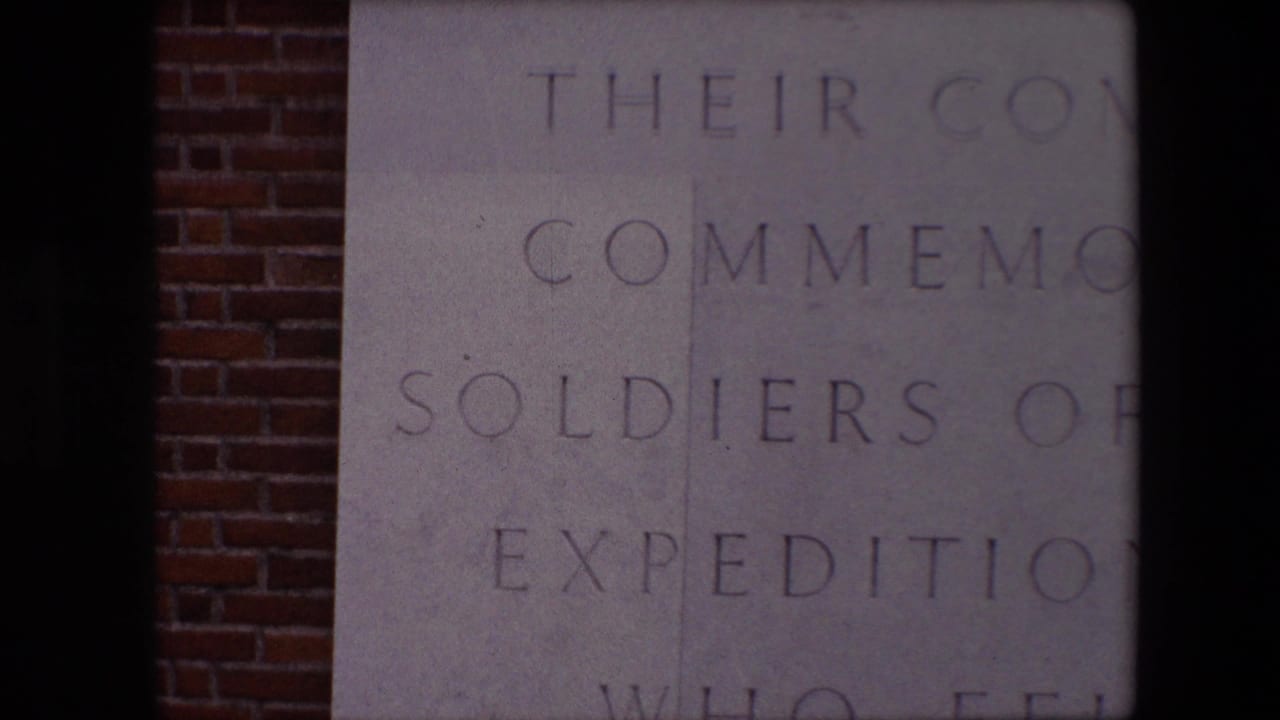 1967 Calais footage showing a close, partial view of engraved memorial text on pale stone, with red brick visible along the left edge.