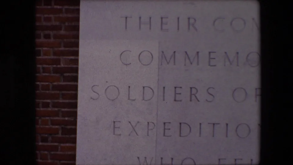 1967 Calais footage showing a close, partial view of engraved memorial text on pale stone, with red brick visible along the left edge.