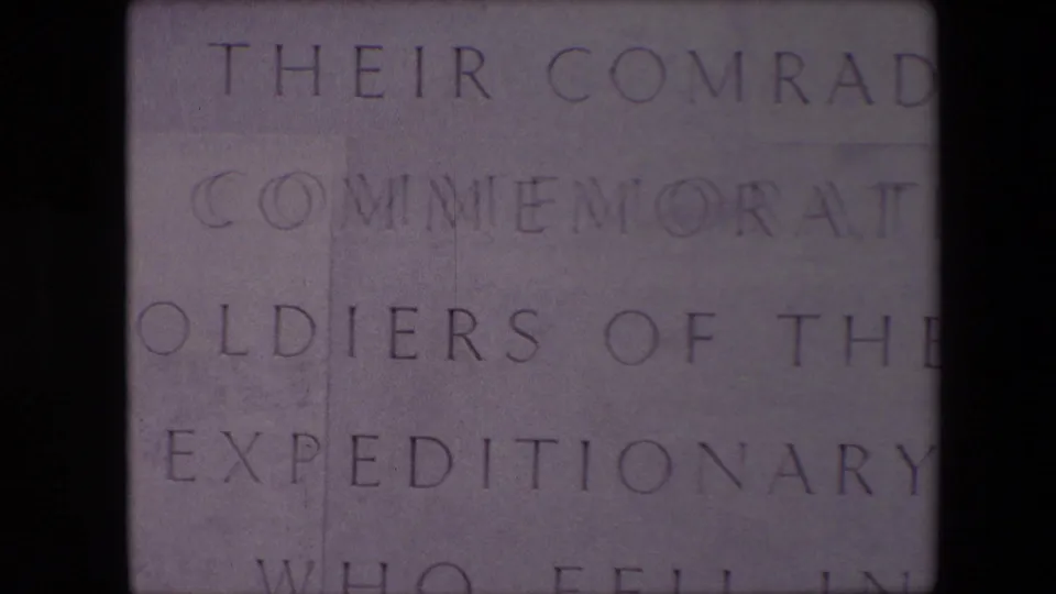 Close 8mm frame of the Calais memorial inscription, partially obscured by a dark vertical band through the center of the view.