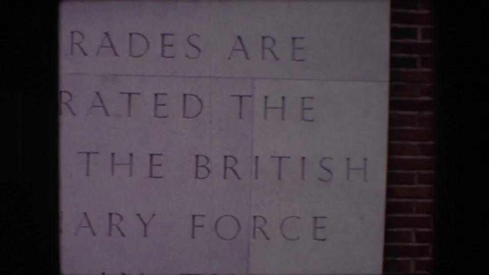 Final close view of the Calais memorial plaque, with partial engraved wording on pale stone and red brick visible at the right edge.