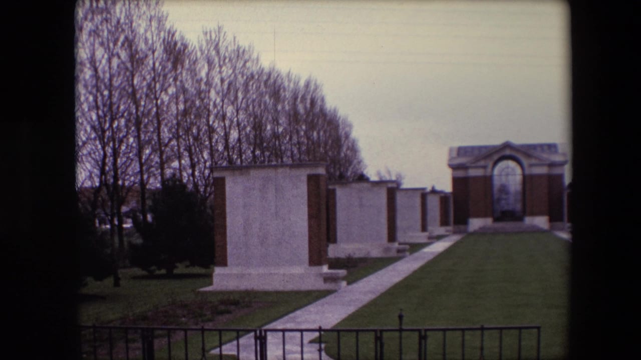 Memorial lawn with pale gravestones, a path, and an arched structure beyond.