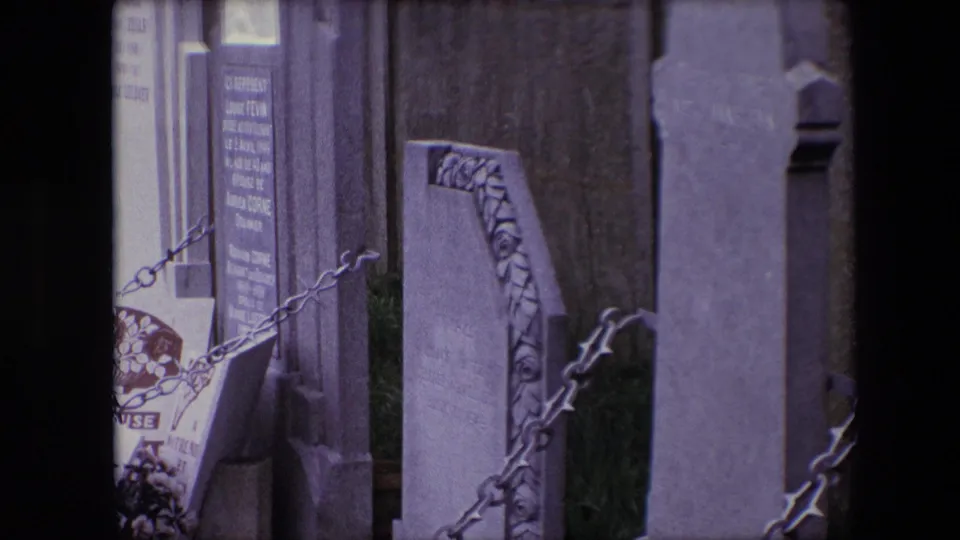 1967 Calais cemetery view with upright stone markers, chain railings, a decorative grave surround, flowers, and a wall behind the plots.
