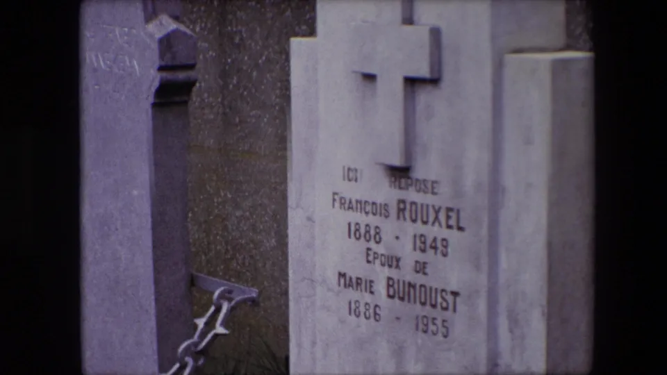 1967 Calais cemetery frame showing a cross-shaped headstone inscribed for François Rouxel and Marie Bunoust, with adjacent stone markers and chain railings.