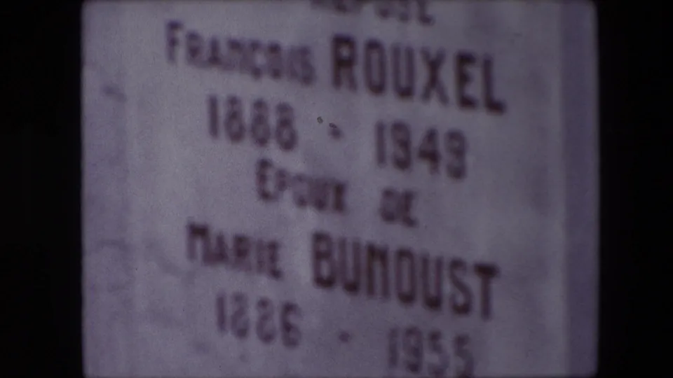 Soft-focus 1967 home-movie frame of the gravestone text for François Rouxel and Marie Bunoust, with the lower dates partly blurred.