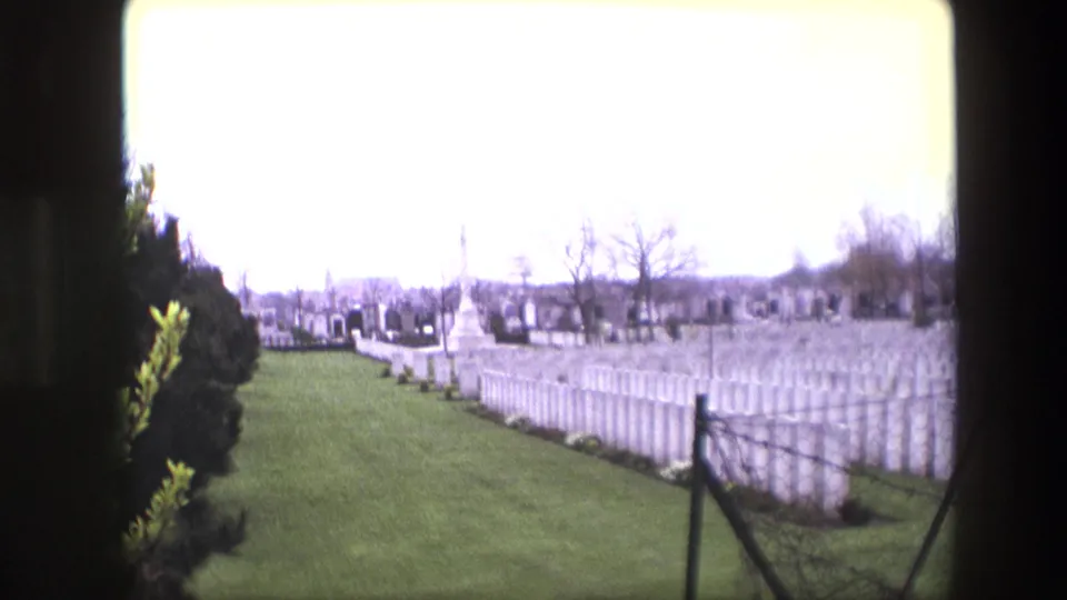 Wide 1967 Calais cemetery view showing rows of white headstones, green grass, trees, and a central monument under a bright overcast sky.
