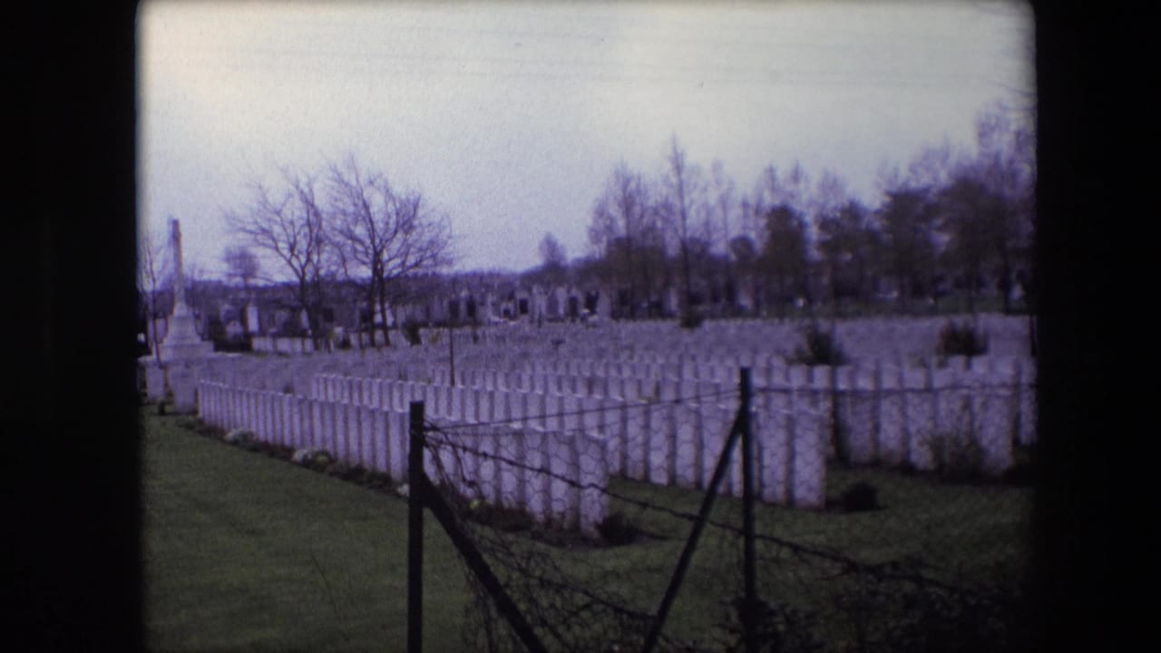 Calais, France, 1967 8mm frame looking across uniform white headstones from behind a dark wire fence, with leafless trees and distant grave markers in the background.