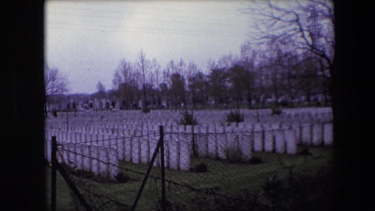 1967 Calais, France 8mm frame showing rows of white military cemetery headstones behind chain-link fencing and barbed wire under bare trees.