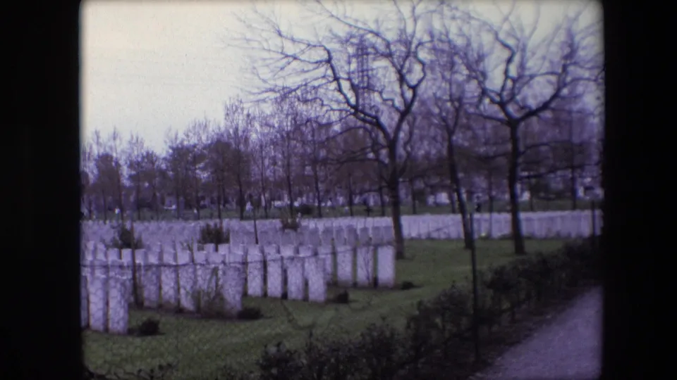 Soft 8mm frame from Calais in 1967 showing a cemetery field of white military headstones, bare trees, grass, and partial film-frame edges.