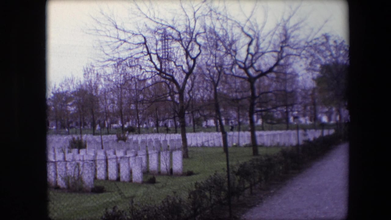 1967 Calais, France home-movie frame showing white cemetery headstones, grass, leafless trees, hedges, and a path under an overcast sky.