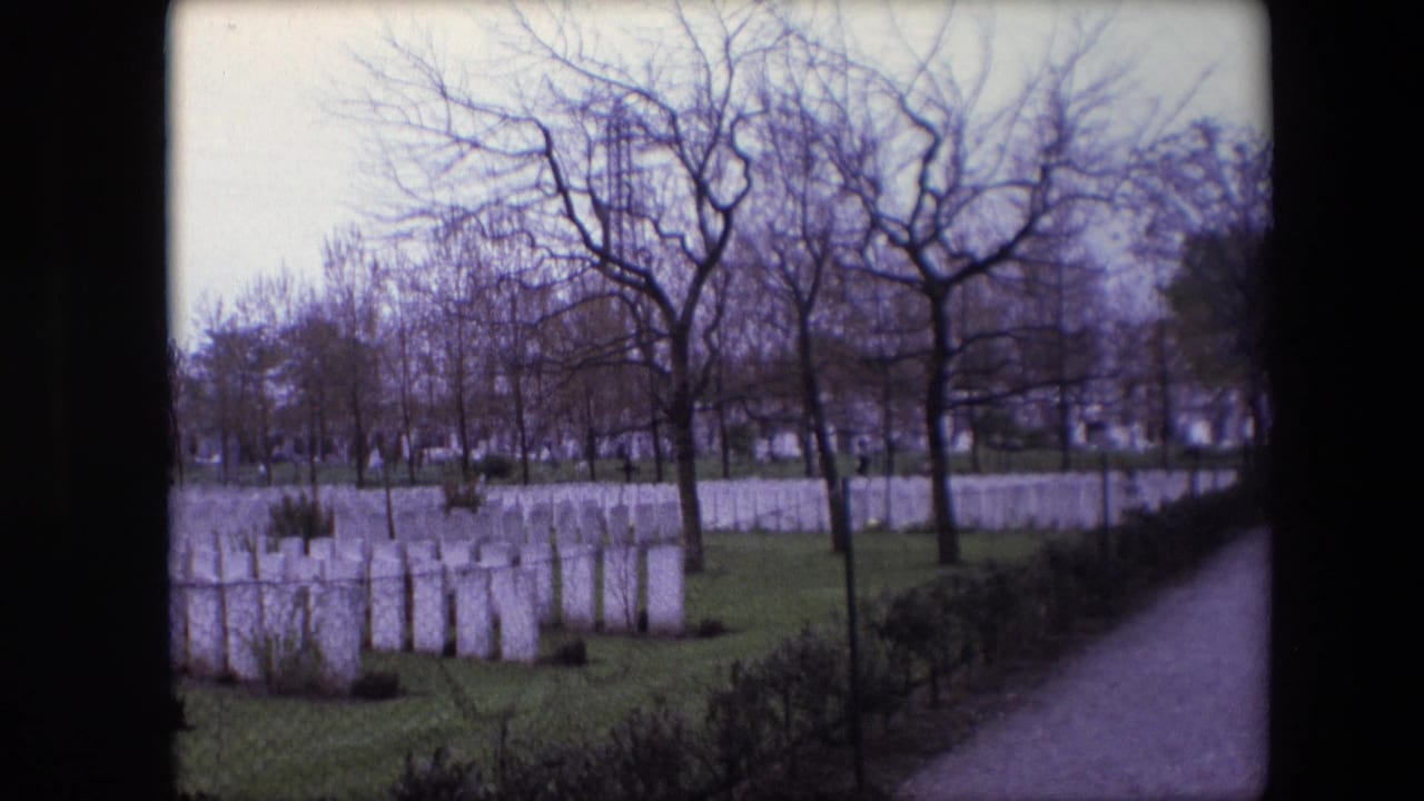 1967 Calais, France frame with rows of white headstones, bare tree branches, green cemetery lawn, hedges, and a path along the right edge.