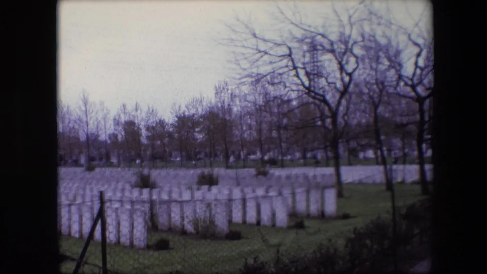 1967 Calais, France frame showing white cemetery headstones, leafless trees, grass, a boundary fence or post, hedges, and dark 8mm frame edges.