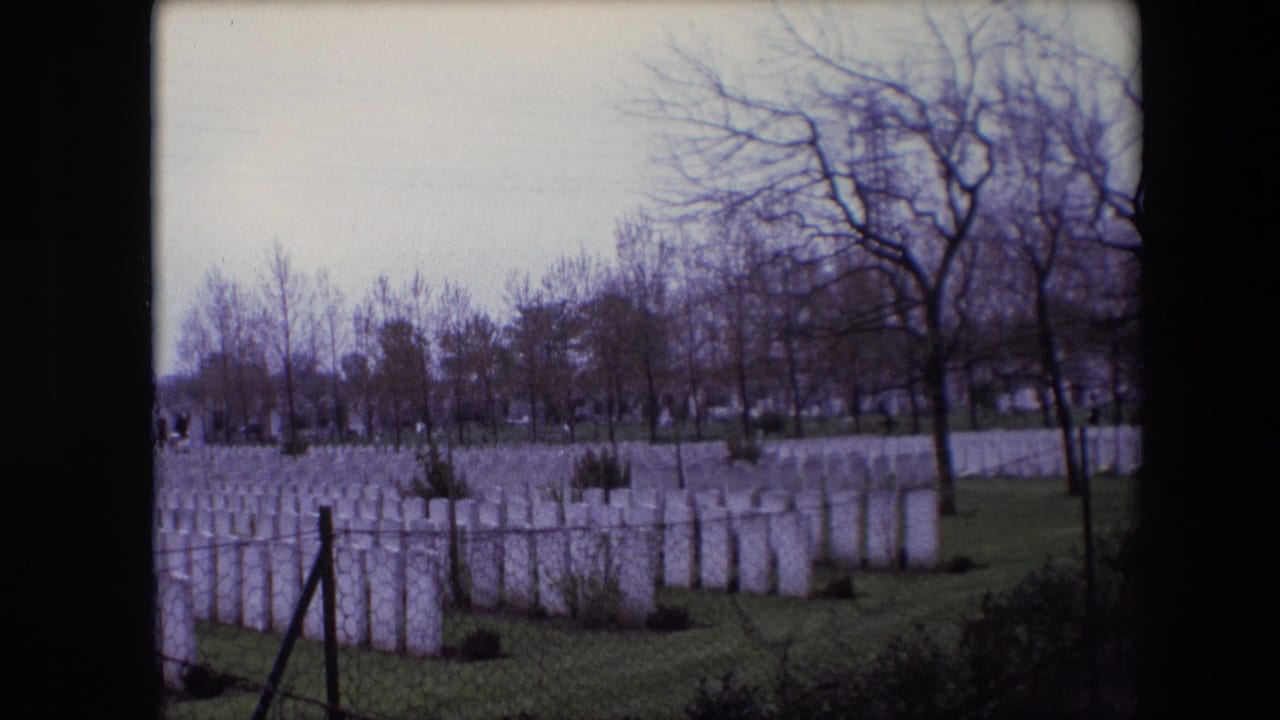 1967 Calais home-movie view of a military cemetery with white headstones, grass, a wire fence, and leafless trees beneath an overcast sky.