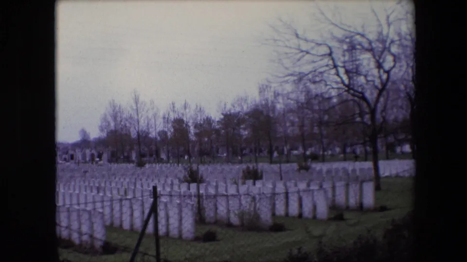 A 1967 Calais cemetery frame shows repeating rows of white headstones, winter-bare trees, grass, and a foreground fence line.