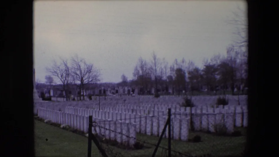 Final 1967 Calais frame shows the cemetery from a slightly shifted angle, with white headstones, a wire fence, bare trees, and a muted cloudy sky.