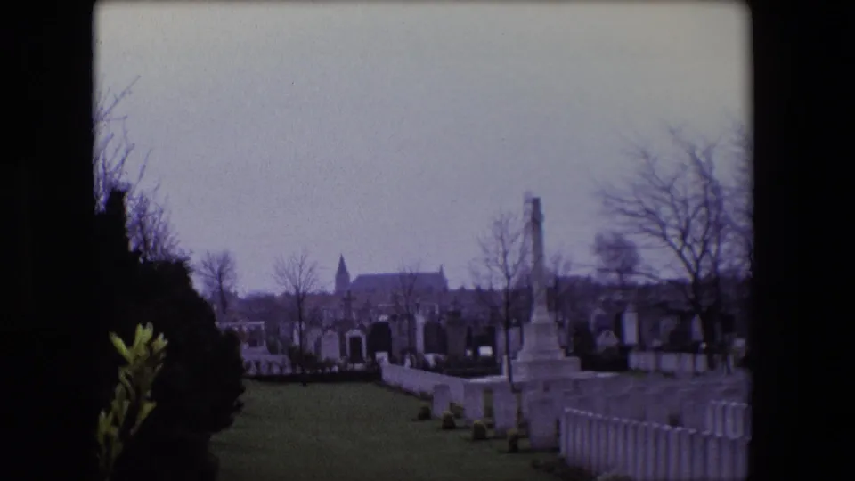 Calais, France cemetery scene from 1967 showing rows of white headstones, a distant church steeple, bare trees, and memorial structures.