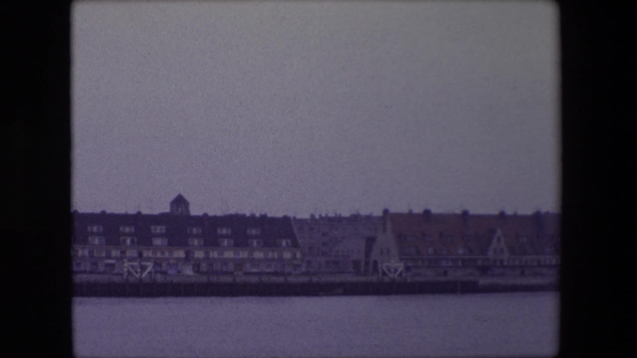 1967 Calais riverfront or harborfront buildings seen from across the water, with a dark roofline, small tower form and pale winter sky.