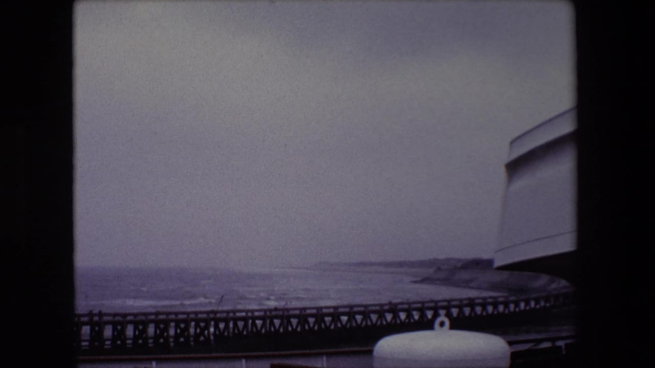 Choppy water and a dark pier under an overcast sky, with a white cylindrical object in the foreground.