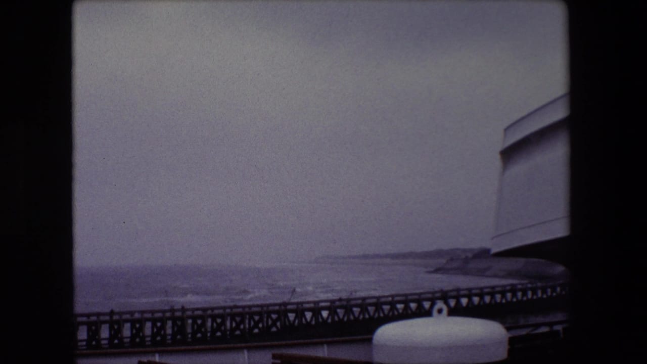 1967 Calais frame with a long pier crossing the lower view, gray Channel water, a low distant coast, and ship or pier hardware in the foreground.