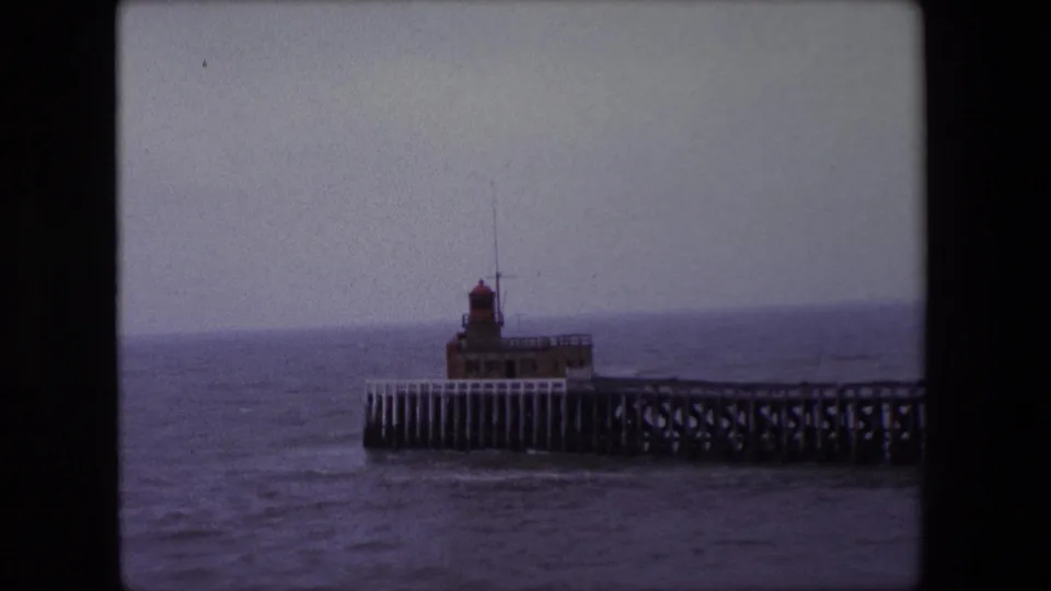1967 Calais 8mm frame showing the pier structure and lighthouse from a slightly lower framed view, with open sea behind it.