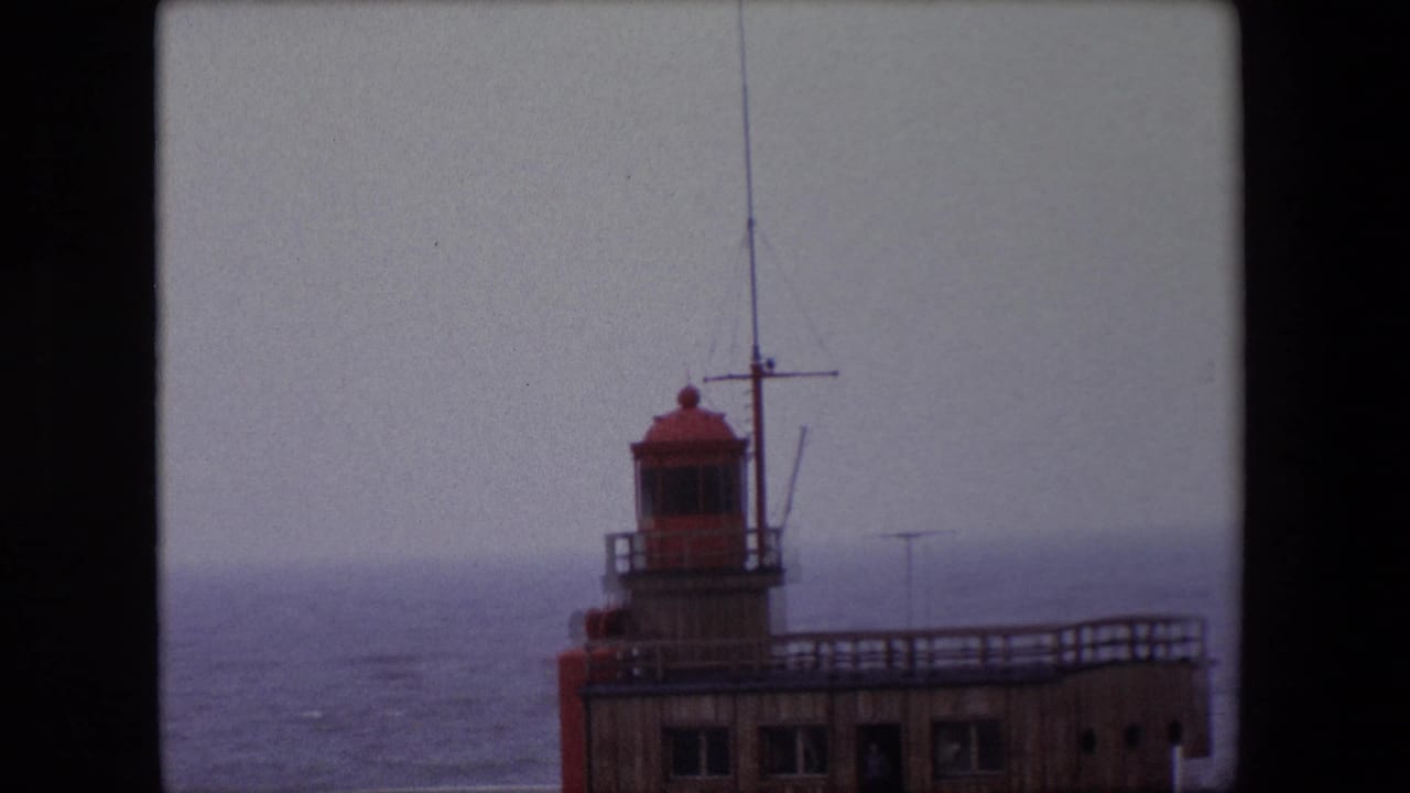 Closer view of the lighthouse lantern room and pier railing beside the sea.