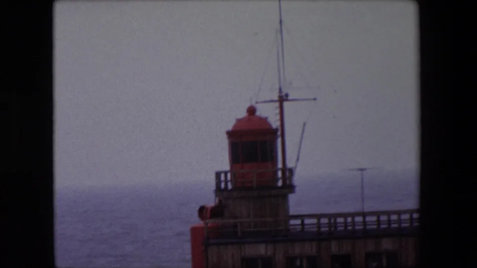 1967 Calais 8mm frame with the lighthouse lantern room, mast, railing, and muted sea visible through soft home-movie exposure.