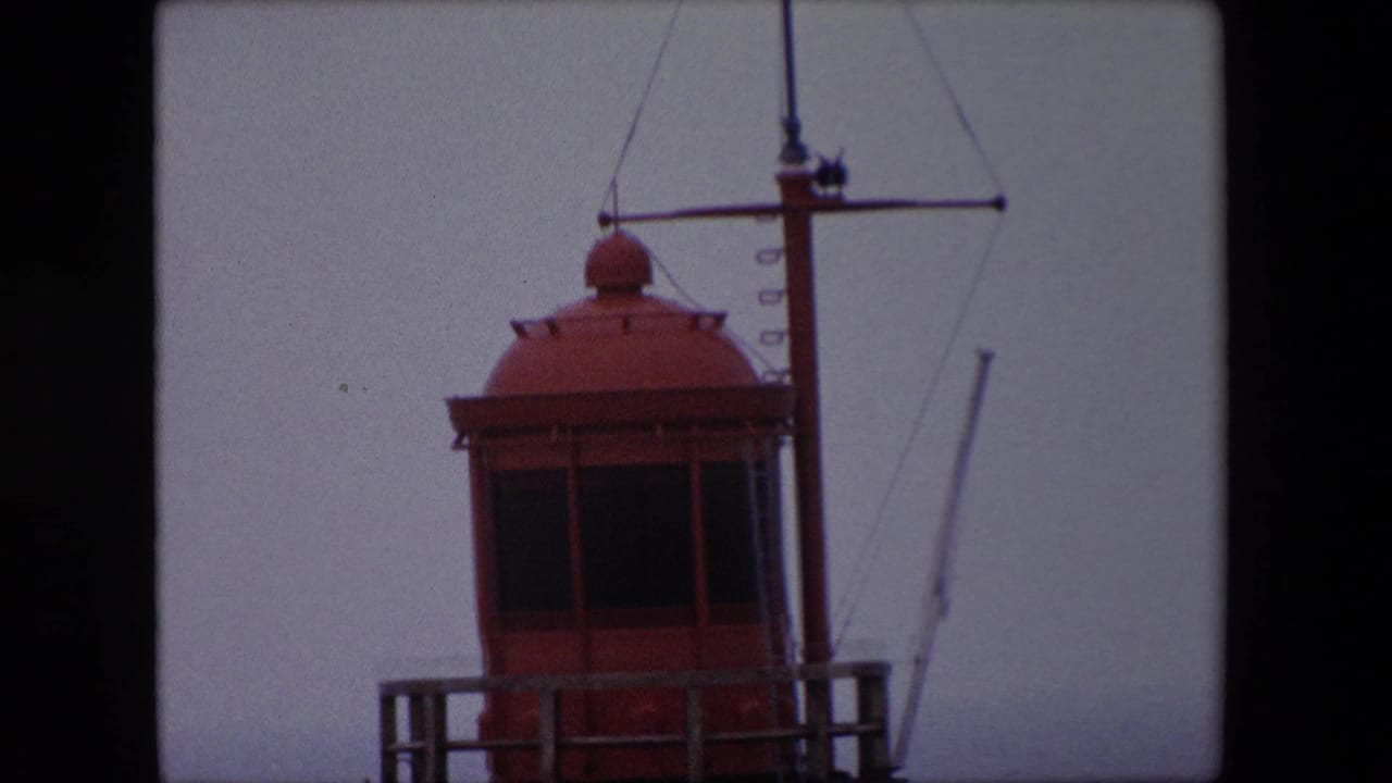 Red lighthouse top cropped beside a mast and rigging in hazy light.