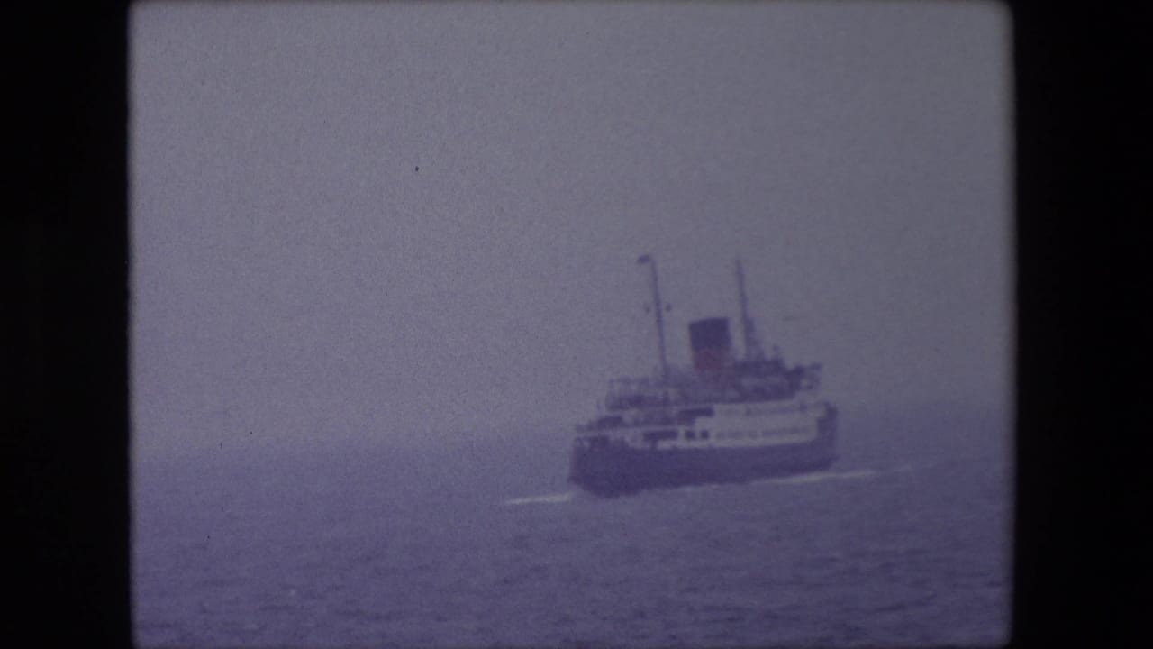 A large passenger ship appears at sea off Calais, France, in 1967, seen through haze in a soft purple-tinted 8mm frame.