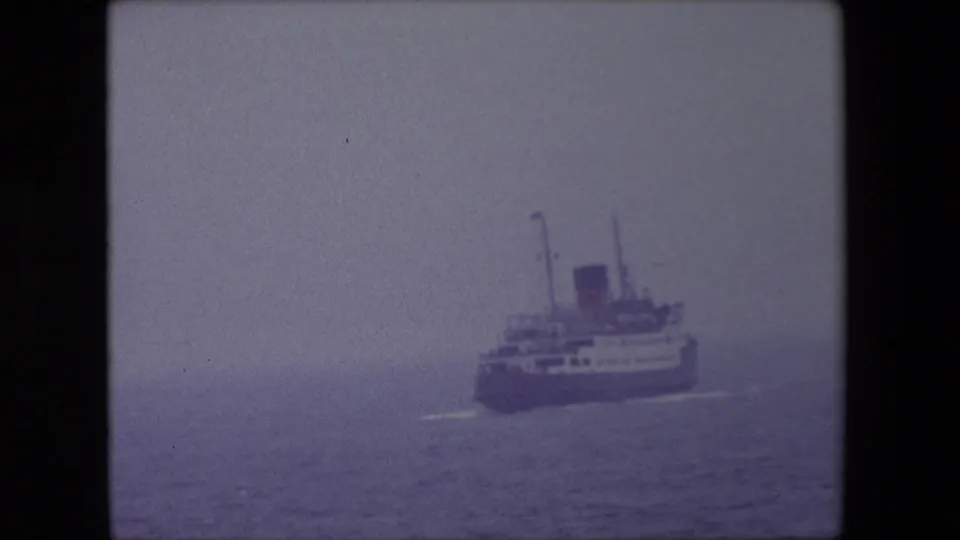 A large passenger ship appears at sea off Calais, France, in 1967, seen through haze in a soft purple-tinted 8mm frame.