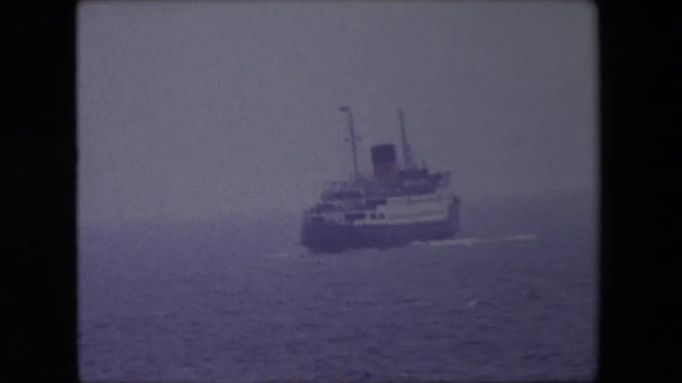 A mid-century passenger vessel is framed low over the water in this 1967 Calais home-movie shot, with the sea and sky divided by dense haze.