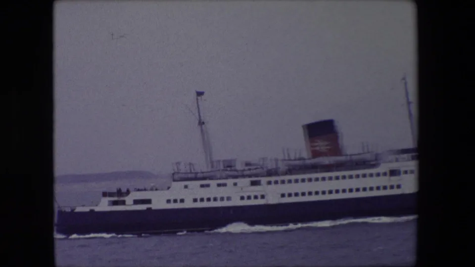 Side view of the 1967 Calais ferry footage, with rows of windows, a mast, and a marked funnel visible as the ship moves through calm sea.