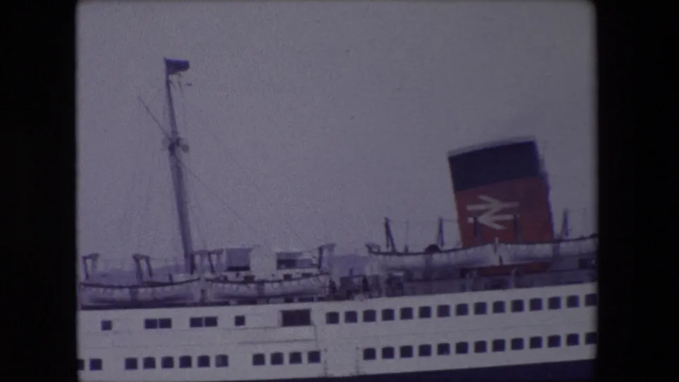 Tight home-movie frame of the 1967 Calais passenger ferry emphasizing the mast, funnel logo, upper railings, and stacked rows of windows.