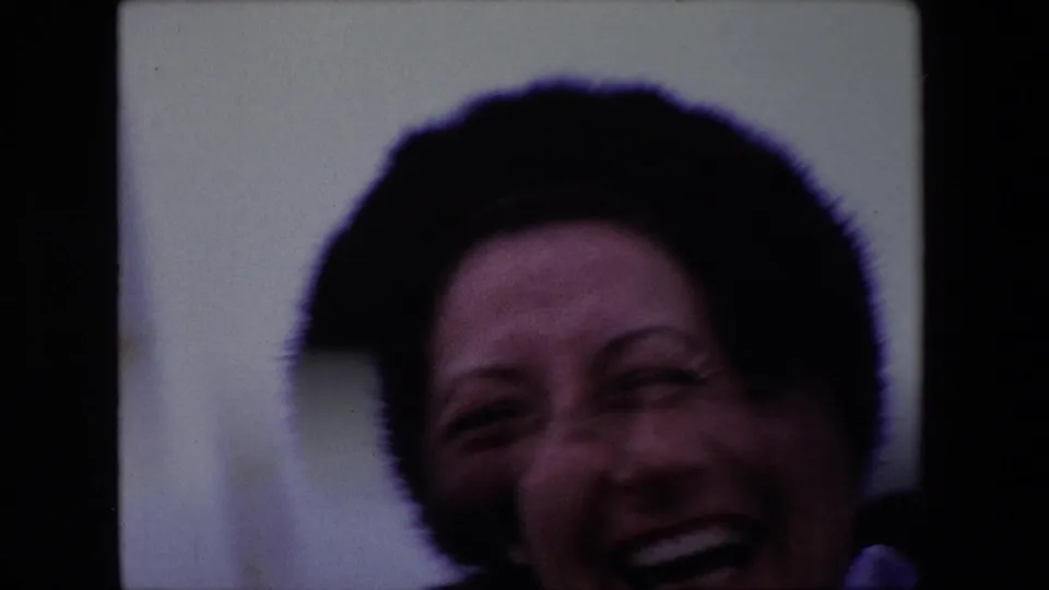 A close, soft-focused 1967 Calais frame shows the woman laughing toward the camera, with her dark fur hat and face partly cropped by the home-movie framing.